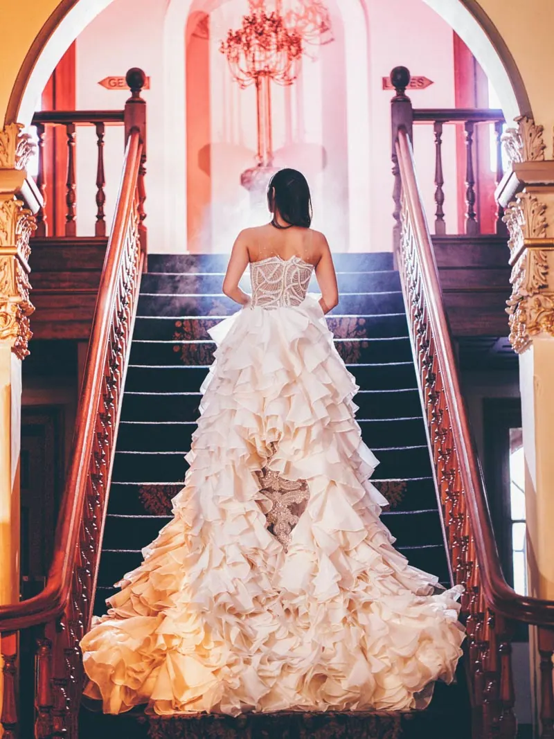 A bride in her bespoke ruffled Catherine Colubriale gown on a staircase
